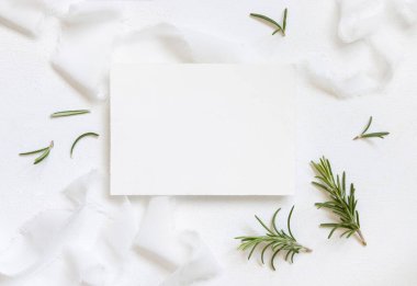 Beyaz ipek kurdelelerin yanındaki boş kart ve biberiye yaprakları üst manzara, düğün modeli. Yatay kartlı ve aromatik yapraklı romantik bir sahne. Sevgililer Günü, Bahar veya Anneler Günü konsepti