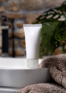 Damardaki beyaz krem tüpü yeşil bitki ve taş duvara karşı kahverengi havluların yanında lavabo açılır. Yüz veya vücut bakımı için doğal kozmetik ürünü