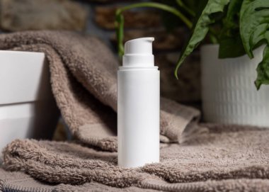 Kahverengi havluların üzerinde beyaz krem pompa şişesi. Lavabonun yanında ve banyoda yeşil bitki. Kapatın, ambalaj modeli. Erkeklerin cilt bakımı için doğal kozmetik ürünleri