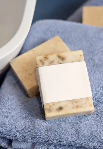 stock image Beige soap bars with blank label on blue towels near vessel sink in bathroom, close up, brand packaging mockup. Natural handmade hygiene product