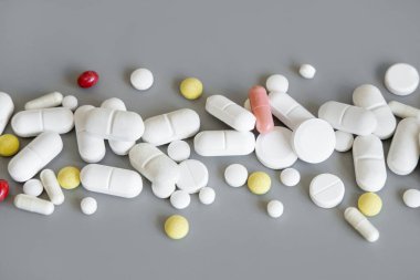 Beyaz kırmızı ve sarı tıbbi kapsüllerin karışımı ve haplar griye yakın bir çizgi üzerinde. Tıbbi tedavi için. Beslenme takviyeleri ve vitaminler alıyor. Çeşitli ilaç ürünleri.