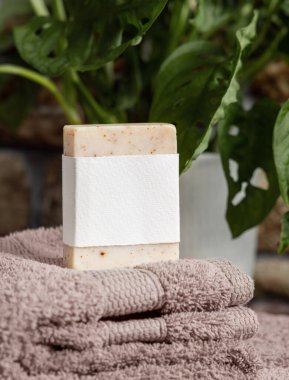 Açık kahverengi havlular üzerinde boş etiketli sabun barı banyoda yeşil fabrikanın yanında, yakın plan, marka ambalaj modeli. Erkekler için hijyen ürünü