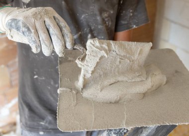 Kirli eldivenli bir zanaatkar metal bir malaya sıva, harç ya da çimento koyar. İnşaat veya yenileme sürecinde giysi üzerinde toz ve alçı olan gri gömlekli adamlar.