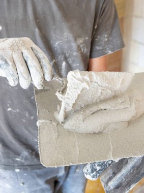 Kirli eldivenli bir zanaatkar metal bir malaya sıva, harç ya da çimento koyar. İnşaat veya yenileme sürecinde giysi üzerinde toz ve alçı olan gri gömlekli adamlar.