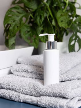 Banyodaki damar havlusunun yanında açık gri katlanmış havlular üzerinde beyaz krem pompa şişesi. Kapatın, ambalaj modeli. Yüz veya vücut bakımı için doğal kozmetik ürünü