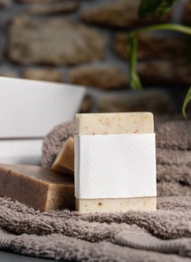 Açık kahverengi havluların üzerinde boş etiket olan sabun barı, banyodaki yeşil bitki ve damar havzasının yanında, yakın plan, marka ambalajlama modeli. Erkekler için hijyen ürünü