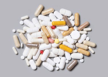 Beyaz, bej, kırmızı ve sarı tıbbi kapsüllerin karışımı ve haplar gri üstte. Tıbbi tedavi için. Beslenme takviyeleri ve vitaminler alıyor. Çeşitli ilaç ürünleri.