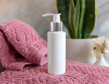 Banyoda yeşil fabrikanın yanında pembe katlanmış havlular üzerinde beyaz krem pompa şişesi, yakın çekim, kozmetik ambalaj modeli. Kişisel bakım için doğal erkek yüz kremi