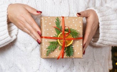 Elinde Noel hediyesi olan beyaz örülü süveter giymiş bir kadın. Paketli ve süslü hediyeli kırmızı tırnaklı kız. Sıcak tatil ortamı