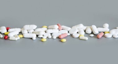 Beyaz kırmızı ve sarı tıbbi kapsüllerin karışımı ve haplar griye yakın bir çizgi üzerinde. Tıbbi tedavi için. Beslenme takviyeleri ve vitaminler alıyor. Çeşitli ilaç ürünleri.