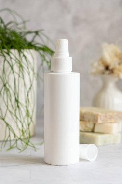 Beyaz sprey kozmetik şişe beyaz mermer üzerinde saksı yeşili bitki ve sabun barları karşı banyoda, yakın çekim, ambalaj modeli. Yüz bakımı, toner veya mikiler için doğal ürün