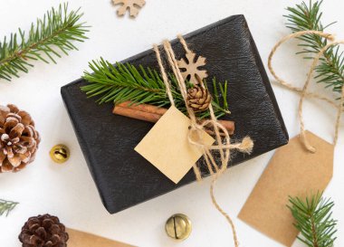 Noel kare hediye etiketli siyah hediye, köknar ağacı dalları, çam kozalakları ve tatil süslemeleri, üst manzara. Kış yatağı, Mockup, kopyalama alanı, tatil atmosferi