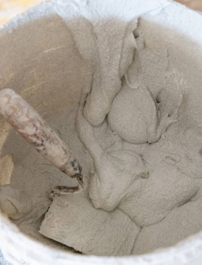 Kirli yüzeyinde çimento ya da alçı olan, içinde mala olan, çimento kalıntılarıyla kaplı bir kova, üst manzara. İnşaat veya yenileme süreci