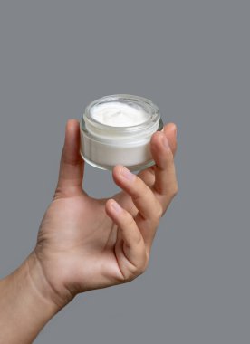 Kadın el krem kavanozunu gri arka planda tutuyor. Yüz bakımı için doğal ürün, günlük cilt bakımı. Kozmetik kutusu açıldı. Spa ve Sağlık Konsepti