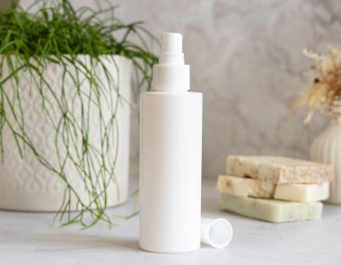 Beyaz sprey kozmetik şişe beyaz mermer üzerinde saksı yeşili bitki ve sabun barları karşı banyoda, yakın çekim, ambalaj modeli. Yüz bakımı, toner veya mikiler için doğal ürün