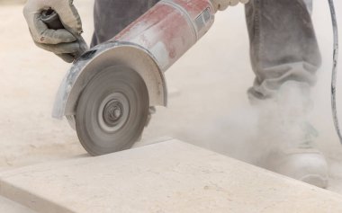 Marangoz, iskelelere karşı mermer kesiyor. İnşaat sırasında tozlu gri iş kıyafetleri ve beyaz miğfer giyen adamlar.