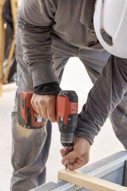 Marangoz inşaat malzemesi veya ahşap mobilya üretmek için tahta tahtada çalışıyor. Ustabaşı profesyonel elektrik kablosuz tornavida kullanıyor. ÇEVİRİ