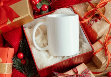 Kırmızı örgü süveterin yanındaki hediye kutusunda beyaz boş kahve kupası ve ışıklara karşı Noel süslemesi ve paketlenmiş hediyeler, fotokopi alanı. Sıcak kış ailesi atmosferik taklidi