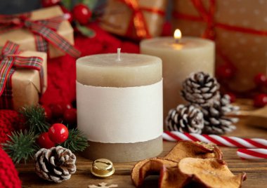 Kırmızı örgü süveterin yanında boş etiketli sütun mumları ve ışıklara karşı Noel dekorasyonu ve paketlenmiş hediyeler, kopyalama alanı. Sıcak kış aile atmosferi. Tatil zamanı.