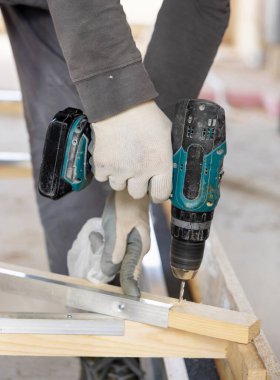 Marangoz inşaat malzemesi veya ahşap mobilya üretmek için tahta tahtada çalışıyor. Ustabaşı profesyonel elektrikli matkap kullanıyor. ÇEVİRİ