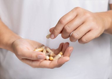 El ele tutuşan bir kadın bej tıbbi kapsülleri beyaz gömleğin üzerine kapatıyor ve parmaklarıyla bir kapsül alıyor. Sağlık hizmetleri için alternatif bitkisel ürünler