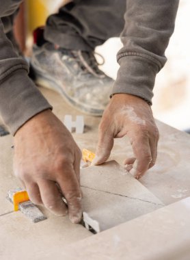Tiler seramik fayansı tozlu ellerle yere seriyor. Seramik fayanslar ve tiler için aletler. Ev tadilatı ya da inşaat sırasında profesyonel bir zanaatkar.