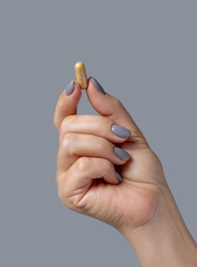Sarı kapsülü tutan kadın el, parmakları gri arka plana yakın plan. Sağlık, tıbbi ve ilaç konsepti, bitkisel alternatif tedavi