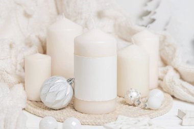 Beyaz örgü süveterin yanında boş etiketli sütun mumu, ahşap Noel dekoru ve ışıklar, kopyalama alanı. Kış atmosferi kırsal ya da İskandinav stiliyle benzer.