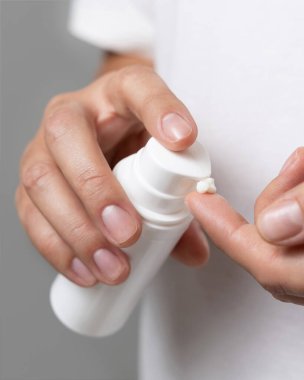 Parmağına el kremi süren ve kozmetik şişeyi Grey 'e karşı tutan bir kadın. Güzellik ya da güzellik salonunda el bakımı.