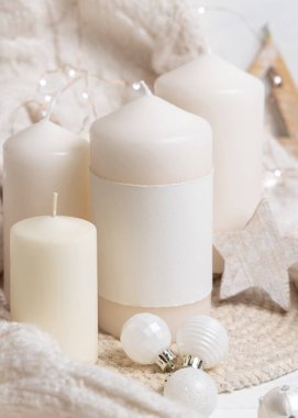 Beyaz örgü süveterin yanında boş etiketli sütun mumları, ahşap Noel dekoru ve ışıklar, kopyalama alanı. Kış atmosferi kırsal ya da İskandinav stiliyle benzer.