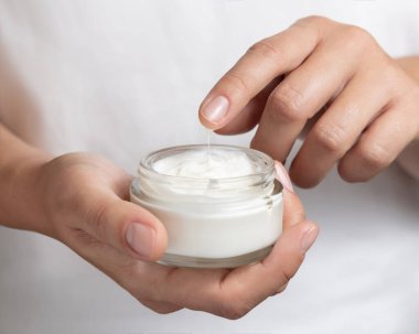Kadının kreme parmağıyla dokunduğu ve elinde doğal nanisürle kozmetik bir kavanozla beyaz gömleği tuttuğu yakın plan. Vücut bakımı için organik kozmetik kavramı