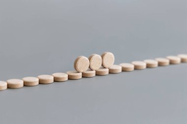 Beige herbal pills in a line on grey close up. Taking natural dietary supplements and vitamins, maca root pills. Alternative medicine clipart