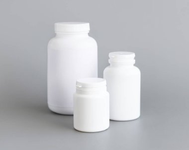 Beyaz plastik hap ya da kapsül şişeleri gri arka plana yakın çekim. Haplarınız ya da kapsülleriniz için ambalaj modeli, Helthcare için bitkisel takviye
