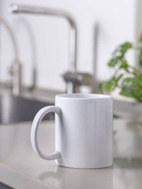 Yeşil bitki, lavabo ve musluk ile mavi modern mutfağın üzerinde gri mutfak masasının üzerinde 11 ons beyaz kahve fincanı kapanıyor. Kopyalama alanı olan tasarım şablonu