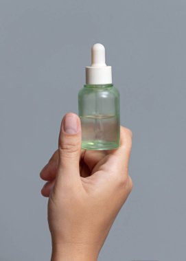 Female hand holding green glass dropper bottle filled with serum or essential oil against grey close up, cosmetic mockup, copy space. Skincare beauty product, minimal composition clipart