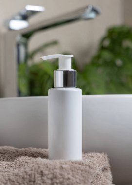 Lavabonun yanındaki kahverengi havlunun üzerinde beyaz krem pompa şişesi ve banyoda yeşil bitki, yakın çekim, kozmetik ambalaj modeli. Kişisel bakım için doğal erkek yüz kremi