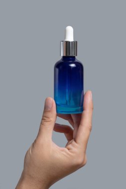 Serum ya da gerekli yağla dolu mavi cam damlatan şişeyi tutan kadın el griye karşı yakın çekim, kozmetik model, kopyalama alanı. Cilt bakımı güzellik ürünü, minimum bileşim