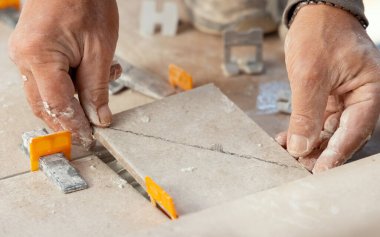 Tiler seramik fayansı tozlu ellerle yere seriyor. Seramik fayanslar ve tiler için aletler. Ev tadilatı ya da inşaat sırasında profesyonel bir zanaatkar.
