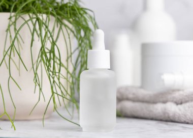 Beyaz mermer üzerine cam damlatan şişe saksı yeşili bitki ve kozmetik ürünlerine karşı banyoda, yakın çekim, ambalaj modeli. Yüz bakımı için doğal ürün - serum ya da öz