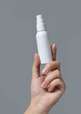 Beyaz kozmetik sprey şişesini Grey 'e karşı tutan kadın el yakın plan, paket maketi, kopyalama alanı. Cilt kremi - losyon ya da krem