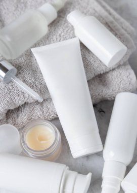Kozmetik şişelerinin yanındaki gri katlanmış havluya beyaz krem sıkma tüpü, üst görünüm, maket. Günlük güzellik rutini ya da spa prosedürleri için kişisel bakım ürünleri