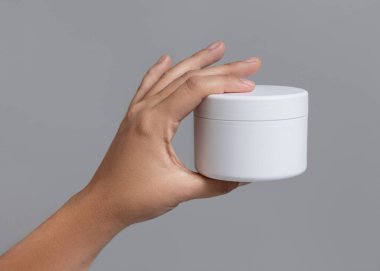 Beyaz, boş krema kavanozunu gri arka planda tutan bir kadın. Yüz bakımı için doğal ürün. Kozmetik konteynır modeli. Spa ve Sağlık Konsepti
