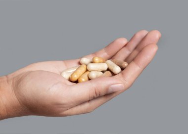 Gri arka plan üzerinde kapalı kapaklı kadın eli ve karışık bej kapsüller. Sağlık hizmetleri için çeşitli ilaç ürünleri