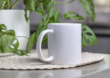 Mavi yeşil bitki ve modern iç mekan üzerinde gri masanın üzerinde 11 ons beyaz kahve fincanı yakın plan, model. Kopyalama alanı olan tasarım ya da reklamcılık için şablon