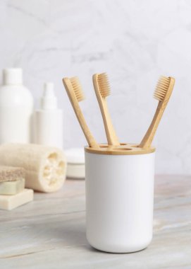 Çevre dostu ahşap bambu diş fırçaları banyoda beyaz bir bardakta, doğal kozmetik ürünlerine karşı. Sıfır atık kavramı, kişisel bakım ve hijyen ürünleri
