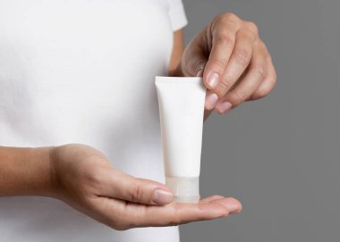 Close up of woman in white t-shirt holding blank squeeze cream tube close up, cosmetic mockup, copy space. Skincare beauty product. Female hands with natural nails clipart