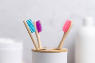 Çevre dostu renkli bambu diş fırçaları banyoda beyaz bir bardakta doğal kozmetik ürünlerine karşı, sahte. Sıfır atık kavramı, kişisel bakım ve hijyen ürünleri
