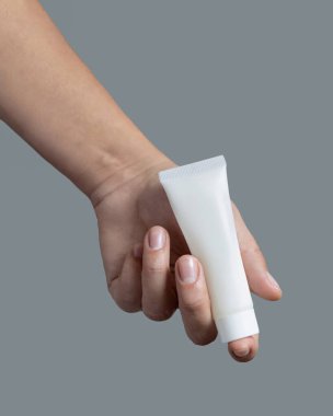 Beyaz sıkma krem tüpünü, gri kaplama kozmetik paket modellemesine karşı tutan kadın el, kopyalama alanı. En az bileşime sahip cilt bakımı ürünü