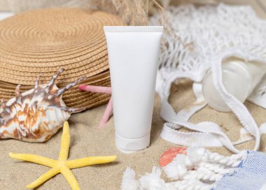 Kumsalda beyaz, boş bir krem tüpü, çanta, havlu, deniz yıldızı ve deniz kabukları, yakın çekim. Güneş kremi kozmetikleri