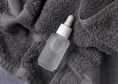 Clear glass dropper bottle with pipette on dark grey towel closeup, brand packaging mockup, copy space. Natural handmade cosmetic product for facecare and spa procedures - serum or essence clipart